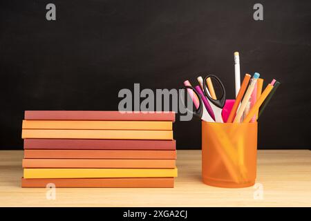 Stapel von Büchern und Büromaterial auf Holztisch und Tafel im Hintergrund. Speicherplatz kopieren Stockfoto