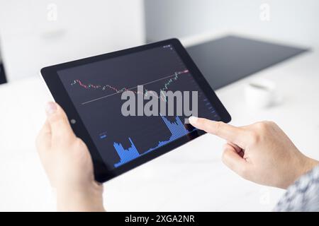 Frau, die in einer modernen Küche ein digitales Tablet mit Börsenchart hält. Trading at Home-Konzept Stockfoto