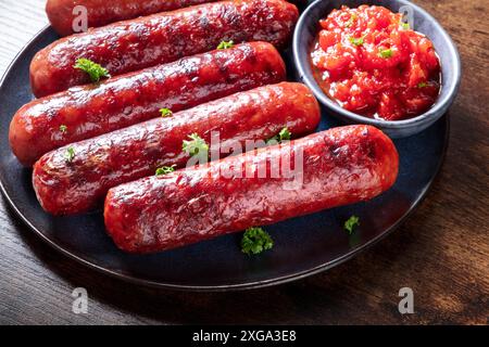 Gegrillte Würstchen mit Ketchup, eine Nahaufnahme auf einem dunklen rustikalen Holztisch. Wiener Bratwurstportion auf einem Teller Stockfoto