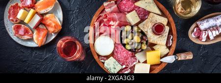 Italienisches Antipasti- oder spanisches Tapas-Panorama auf schwarzem Hintergrund. Gourmet-Aufschnitt- und Käseplatte auf schwarzem Hintergrund, von oben aufgenommen mit Stockfoto