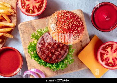 Rindfleisch-Burger-Zutaten, darüber liegende flache Schuss mit Pommes frites. Hamburger und Kartoffeln, von oben auf ein Holzbrett geschossen Stockfoto