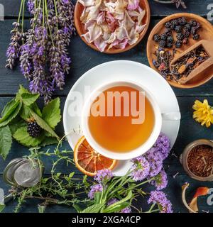 Eine Tasse Tee mit trockenem Obst, Blumen und Kräutern auf einem dunklen rustikalen Holzhintergrund, quadratische Aufnahme über dem Kopf Stockfoto