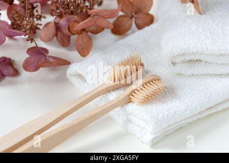 Zwei Bambuszahnbürsten auf weißen Handtüchern mit Blumen im Hintergrund, umweltfreundlicher Lifestyle Stockfoto