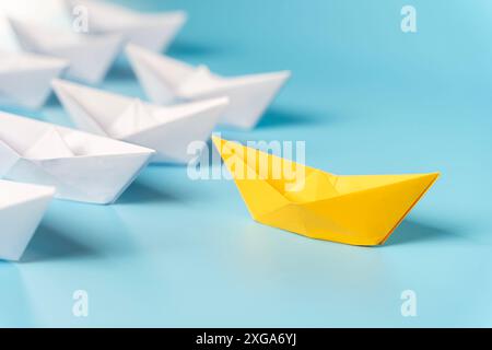 Führungskonzept, gelbes Führungsboot, das schwarze Boote führt, auf blauem Hintergrund mit leerem Kopierraum. Siegerschiff aus rotem Papier. Neue Ideen, Kreativität und Stockfoto