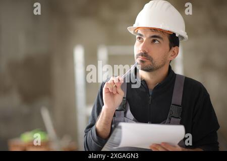 Nachdenklicher Bauarbeiter mit Klemmbrett und Blick über ein Haus Stockfoto