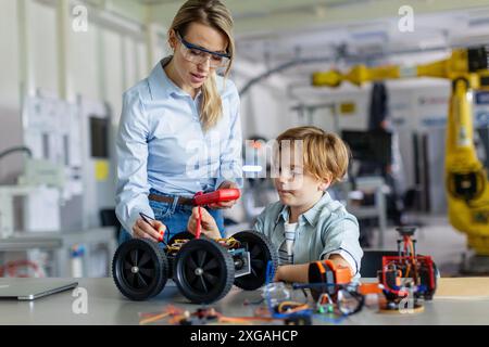 Eine Lehrerin hilft jungen Schülern beim Bau eines Roboterautos im Robotikclub. Kinder, die Robotik in der Grundschule lernen. Wissenschaft Stockfoto