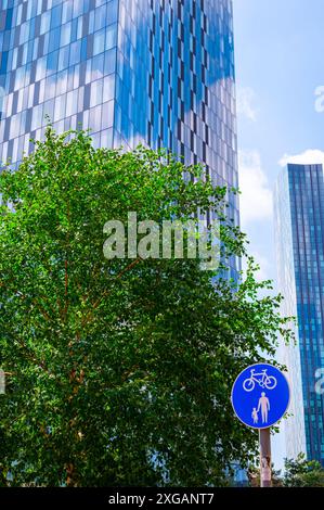 Ein Turm am Deansgate Place, Castlefield, Manchester mit blauem Himmel, einem üppig grünen Baum und einem blauen Radweg-Schild. Stockfoto