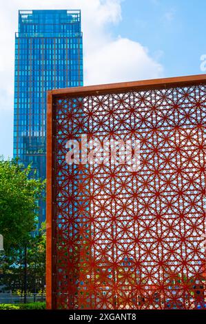 Ein Turm am Deansgate Place, Castlefield, Manchester mit blauem Himmel, einem üppig grünen Baum und einer gemusterten, rostfarbenen dekorativen Metalltafel. Stockfoto