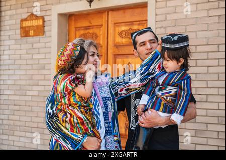 Glückliche usbekische Familie mit Kindern in traditionellen usbekischen Kostümen auf der Straße in der Stadt. Taschkent, Usbekistan - 18. April 2024 Stockfoto