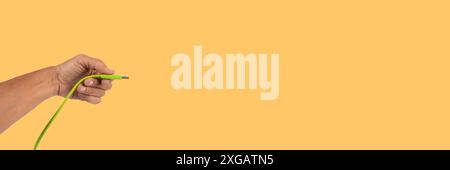 Schwarze männliche Hand, die ein USB-Kabel auf gelbem Hintergrund hält Stockfoto