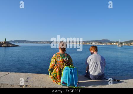 Junges Paar, 25 Jahre alt, im Freien, auf der Hafenmauer, mit Blick auf die Küste der Costa Blanca, Javea, Provinz Alicante, Spanien Stockfoto