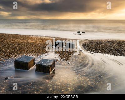 Wellen, die um die Überreste der hölzernen Seeschutzmauern herrinnen. Stockfoto