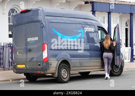 Frau Prime Delivery Fahrer Rückansicht zurück zum geparkten Amazon Ford Van Vervollständigung der Paketzustellung Seite Werbemarke & Logo Devon England UK Stockfoto