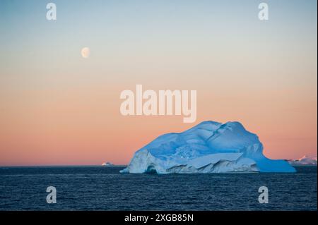 Immer größer werdende Eisberge brechen vom Land ab und machen sich dort auf den Weg ins Meer. Die wunderschönen Kunstwerke aus der Natur tragen ironische Schönheit bei Sonnenuntergang bei Vollmond. Stockfoto