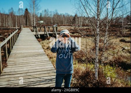 Junge, der Frösche durch ein Fernglas in einem Hochmoor an einem klaren Tag beobachtet Stockfoto