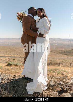 Ehemann und Ehefrau, die sich auf einer Solar-Windkraftanlage umarmen Stockfoto