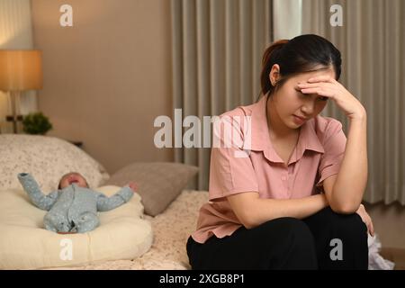 Erschöpfte junge Mutter mit postnataler Depression, die neben ihrem kleinen Sohn im Bett sitzt. Psychische Gesundheitskonzepte Stockfoto