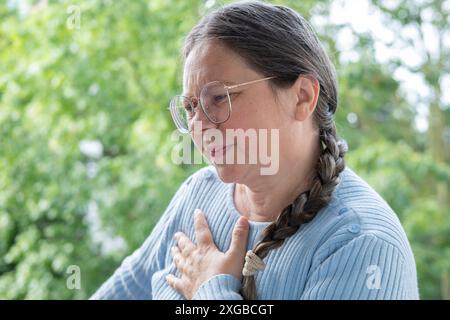 Erkrankte reife Frau schließt Brust, erlebt plötzliche Schmerzen in der Brust, arterielle Hypertonie, Atemnot, Atemprobleme und Stress, se Stockfoto
