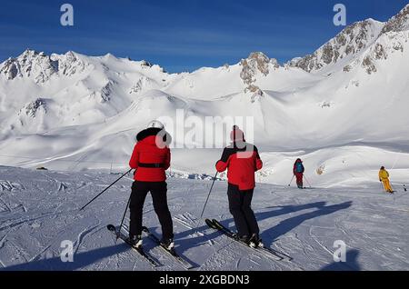 Zwei Skifahrer stehen auf einer Skipiste oberhalb von Tignes in Frankreich bereit, in roten Skijacken abzusteigen und von der Kamera wegzusehen. Stockfoto