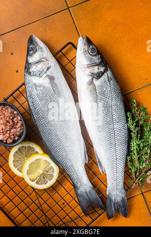 Roher Seebarsch mit Limette und Kräutern. Orangefarbener Hintergrund. Draufsicht Stockfoto