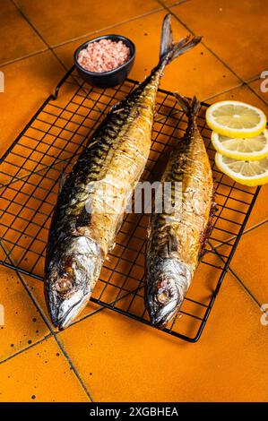 Gebratener Makrelen-Scomber-Fisch mit Zitrone, Kräutern und Gewürzen auf einem Grill. Orangefarbener Hintergrund. Draufsicht Stockfoto