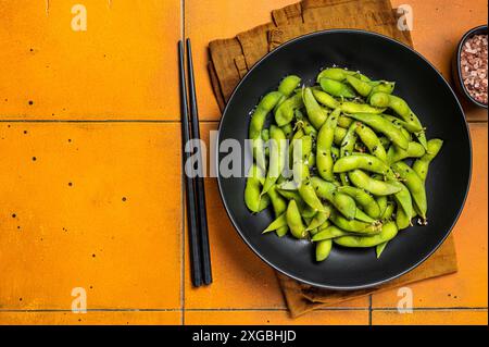 Gekochte Edamame Sojabohnen mit Meersalz und Sesamsamen. Orangefarbener Hintergrund. Draufsicht. Kopierbereich Stockfoto