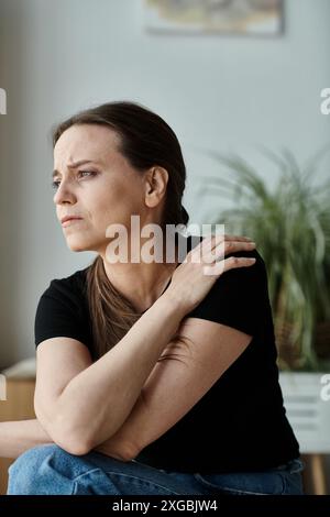 Eine Frau mittleren Alters sitzend, Arm an Schulter, tief in Gedanken. Stockfoto