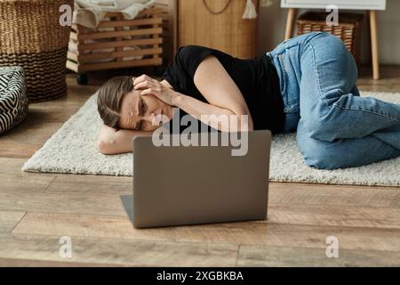 Frau mittleren Alters, die in Not neben dem Laptop liegt. Stockfoto