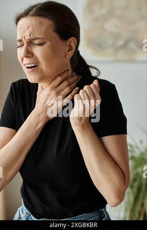 Depressive Frau mittleren Alters zu Hause mit Nackenschmerzen. Stockfoto