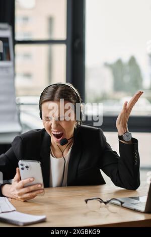 Frau mittleren Alters in Not, die am Schreibtisch sitzt und ihr Smartphone anschrie. Stockfoto