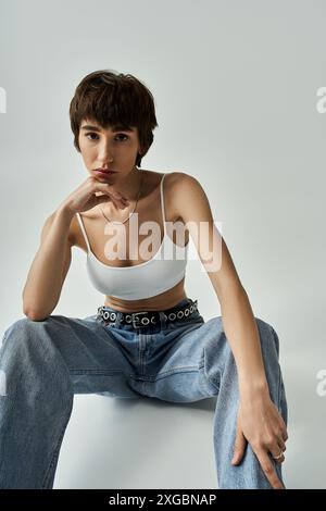 Stilvolle Frau in weißem Oberteil und Jeans, die anmutig auf dem Boden sitzt. Stockfoto