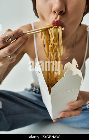 Eine schöne junge Frau in modischer Kleidung, die Nudeln direkt aus einer Schachtel isst. Stockfoto