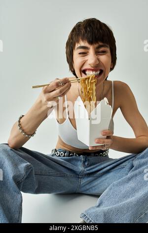 Frau in stilvoller Kleidung schmeckt Nudeln, während sie anmutig auf dem Boden sitzt. Stockfoto