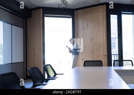 Geschäftsmann, der im Büro steht, das Smartphone benutzt und sich gegen die Wand lehnt, Kopierraum Stockfoto