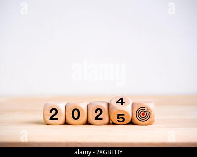 2025 ein frohes neues Jahr mit Zielen und erfolgreichen Bannerkonzepten. Die Kalenderzahlen für 2024 bis 2025 Jahre werden mit dem Zieldart-Symbol auf dem Holzwürfel Blo umgedreht Stockfoto