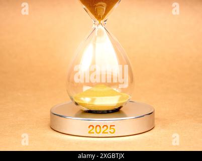 In Kürze für das neue Jahr 2025: Business and Technology Concept. Nahaufnahme Sanduhr mit goldenem Sand innen, auf rundem silberchromchromhaltigem Podium mit 2025 Jahren Stockfoto