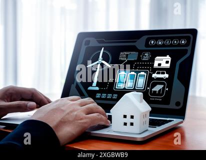 Intelligentes Zuhause – mit dem Konzept für erneuerbare Energien können Sie Ihr Zuhause mit Strom versorgen. Datensystem für erneuerbare Energien und Management Control Display und weißes kleines Haus auf Laptop Stockfoto