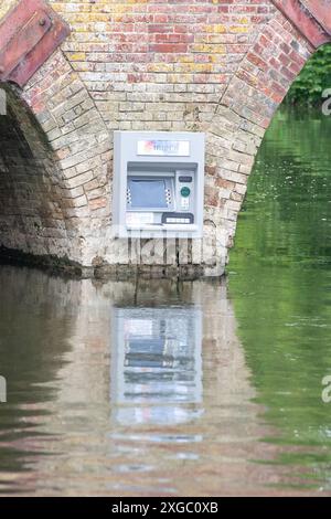 Sonning-on-Thames, Berkshire, Großbritannien. Juli 2024. Ein Streich namens Impro hat an der Wand der Sonning Bridge oberhalb der Themse in Sonning-on-Thames, Berkshire, einen Geldpunkt platziert. Über dem Cashpoint befindet sich ein Impro Solutions Logo. Impro war auch hinter einem Briefkasten, der vor ein paar Monaten an derselben Mauer über der Themse angebracht wurde. Dies hat den Einheimischen viel Spaß bereitet und das Ziel soll darin bestehen, die Aufmerksamkeit auf die Anzahl der Banken zu lenken, die geschlossen werden. Berühmte Bewohner, die Eigentum in Sonning besitzen, sollen George Clooney und der ehemalige P sein Stockfoto