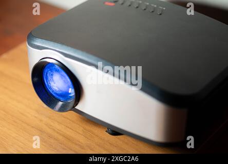 Eine Nahaufnahme eines modernen Digitalprojektors mit blauer Linse auf einer Holzoberfläche. Stockfoto
