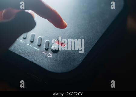 Nahaufnahme einer Person, die den ein-/Ausschalter eines schwarzen elektronischen Geräts mit mehreren Tasten und einem kleinen Display drückt. Stockfoto