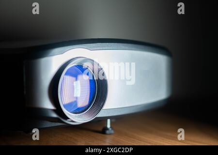 Nahaufnahme eines modernen Digitalprojektors mit blauer Linse auf einer Holzoberfläche. Stockfoto