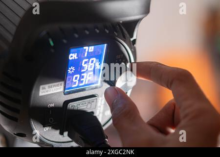 Nahaufnahme einer Hand, die die Einstellungen einer Videoleuchte auf einer digitalen Anzeige anpasst. Auf dem Display werden Kanal, Helligkeitsgrad und Farbtemperatu angezeigt Stockfoto