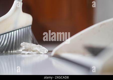 Nahaufnahme eines Besens, der ein zerknittertes Papierpapier in eine Kehrschaufel auf weißem Boden fegt. Stockfoto