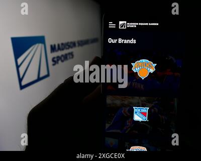 Person, die ein Handy hält, mit Webseite der US-amerikanischen Firma Madison Square Garden Sports Corp. Vor dem Logo. Konzentrieren Sie sich auf die Mitte des Telefondisplays. Stockfoto