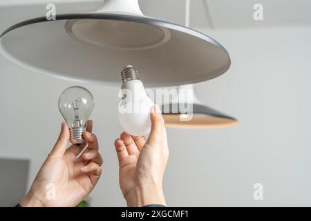 Energiesparende Idee: Asiatische Menschen ersetzen Leuchtstofflampen (CFL) durch neue LED-Lampen. Weibliche Hände Schrauben eine energiesparende LED-Glühlampe ein. Stockfoto