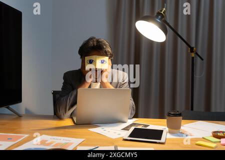 Erschöpfte junge kaukasische Arbeiter haben Stickerpads an den Augen, die in der Nähe des Computers im Büro schlafen. Müder männlicher Angestellter des Millennials schläft ein Stockfoto