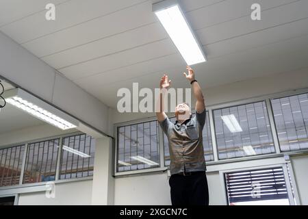 Glücklicher Mann, der zu Hause eine Glühbirne wechselt. Energiesparende Hochwinkellampe in einer weißen Deckenlampe, die Leuchtstofflampen überprüft oder ersetzt Stockfoto