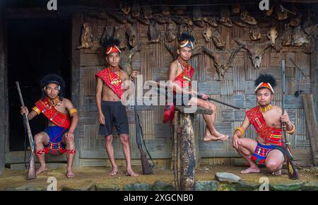 Dieses Bild zeigt junge Konyak-Männer in traditioneller Kleidung, die Gewehre halten, mit einer Kulisse aus Tierschädeln, die ihr Kriegererbe widerspiegeln. Stockfoto