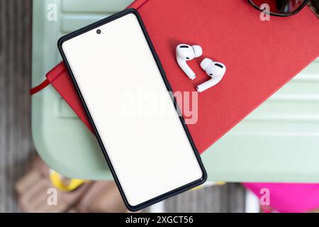 Ein schwarzes Handy sitzt auf einem weißen Holztisch. Das Telefon ist eingeschaltet und der Bildschirm zeigt einen schwarzen Hintergrund mit Ohrstöpseln an. Das Telefon ist umgeben Stockfoto