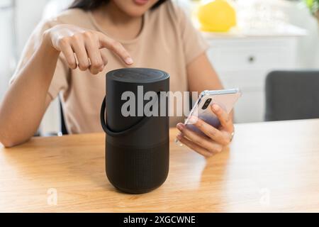 Nahaufnahme eines kabellosen Lautsprechers vor einer Frau, die zu Hause auf einem Schreibtisch sitzt. Frau streamt Musik oder Podcasts von Ihrem Mobiltelefon auf Smart Speaker Stockfoto